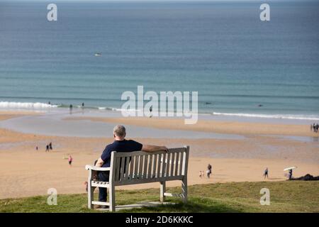 Newquay,Cornwall,18 octobre 2020, UN homme est assis sur un banc de bois regardant les gens profiter du temps chaud lors d'une belle Sunny Day à Fistral Beach, Cornwall. La plage est célèbre car les gens voyagent de tout le pays pour monter sur le célèbre surf.Credit: Keith Larby/Alay Live News Banque D'Images