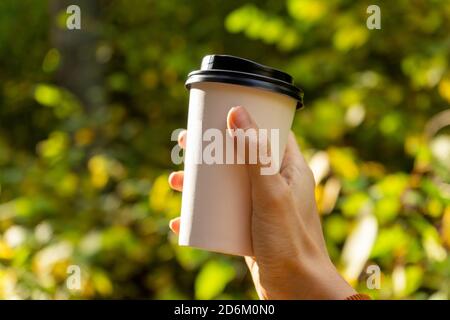 Une jeune femme tient une tasse de café jetable le matin ou le jour ensoleillé. Une femme qui va faire une promenade avec une tasse de café le beau jour d'automne. Banque D'Images