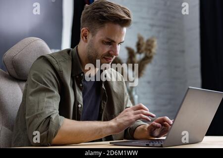 Jeune indépendant travaillant à la maison avec un ordinateur portable. Envoi de SMS, navigation sur Internet. Études en ligne, formation en ligne, travail à distance. Jeunes Banque D'Images