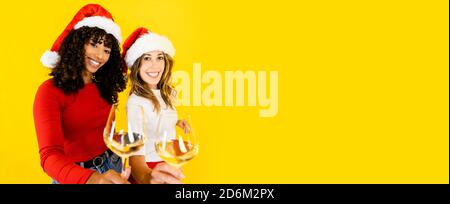 Toaster to Christmas Together indépendamment de la diversité - deux femmes, hispanique noire et caucasienne portant le chapeau de Santa, regardant la caméra tenant un gl Banque D'Images