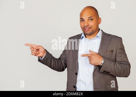 Joyeux jeune homme d'affaires afro-américain souriant avec joie et pointant vers le côté avec des index sur les deux mains tout en regardant dans la caméra. Espace de copie pour votre annonce Banque D'Images