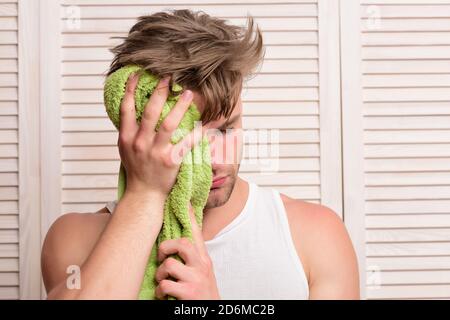 Athlète avec des muscles forts après la douche. Homme avec une serviette verte essuie son visage. Guy avec des cheveux salissants et un visage endormi sur fond de porte en bois. Exercices du matin et concept de style de vie de rafraîchissement Banque D'Images