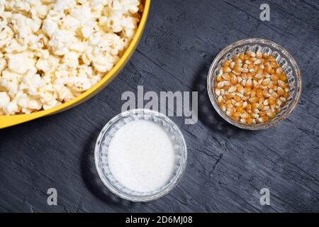 Pop-corn dans un bol jaune à côté des grains de maïs et sel Banque D'Images