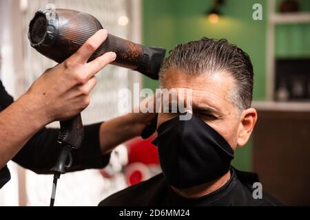 white caucasien barber peignes et souffle-drys cheveux d'un autre homme dans un salon de coiffure pendant la pandémie de coronavirus. ils vont rétro style hipster et nous tous les deux Banque D'Images