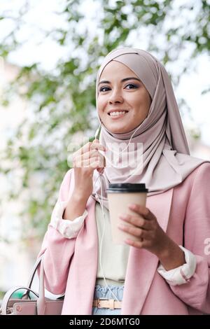 Jeune femme musulmane souriante et magnifique avec un verre de café téléphonant quelqu'un Banque D'Images