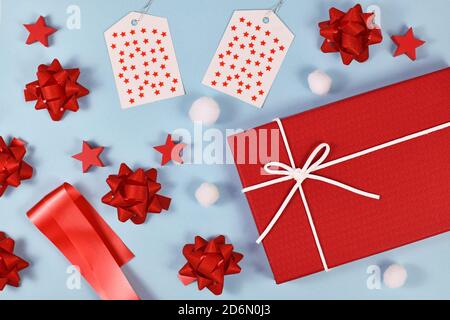 Cadeau de Noël concept d'emballage avec boîte cadeau rouge, rubans, étiquettes cadeau, ornements d'arbre et boules de neige sur fond bleu clair Banque D'Images