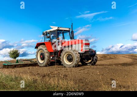 Tracteur agricole rouge cultivant le champ sur ciel bleu. Vieux tracteur rouge dans le champ agricole ; mécanisme. Le tracteur labourage la terre. Semis de la récolteuse Banque D'Images