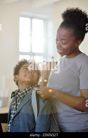 Bonne jeune mère attentive en vêtements décontractés aider son petit fils avec sac à dos Banque D'Images