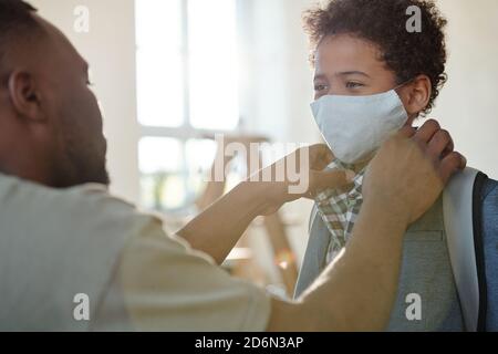 Jeune père redressant chemise collier de son fils avec protecteur masque sur le visage Banque D'Images