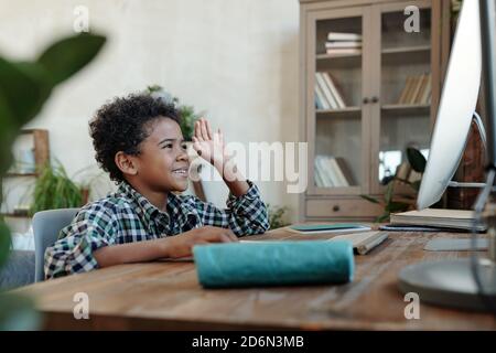 Joyeux petit garçon d'école assis devant l'écran d'ordinateur pendant leçon en ligne Banque D'Images