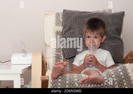 Petit garçon malade avec masque nébuliseur faisant l'inhalation, procédure respiratoire par pneumonie ou toux pour enfant à la maison. Banque D'Images