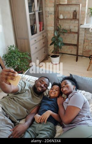 Jeune famille joyeuse de parents affectueux et de leur petit fils faire du selfie Banque D'Images