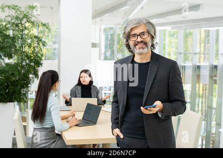 Homme d'affaires mature et réussi en lunettes et costume debout devant de la caméra Banque D'Images