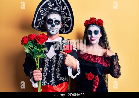 Jeune couple portant la tenue du jour mexicain de la mort roses pointant du doigt vers un individu souriant heureux et fier Banque D'Images