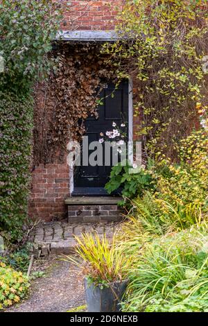 vieille porte de chalet en bois entourée de plantes et de fleurs dans un jardin de campagne avec chemin menant à l'entrée. Banque D'Images