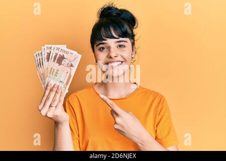 Une jeune fille hispanique détenant 5000 sud-coréenne a gagné des billets souriants contenchez-vous de pointer avec votre main et votre doigt Banque D'Images