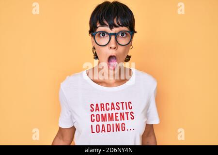 Belle femme brunettte portant des commentaires sarcastique chargement du t-shirt peur et stupéfait avec la bouche ouverte pour la surprise, le visage incrédulé Banque D'Images