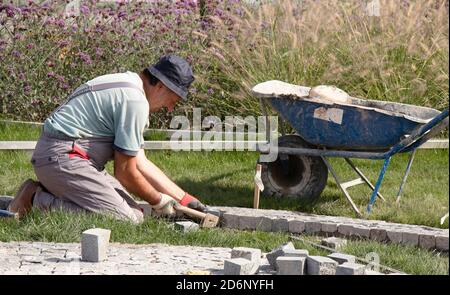 Belgrade, Serbie - 09 octobre 2020: Ouvrier du constructeur qui organise le terrain en granit pavé , pavant la voie piétonne décorative dans le parc de jardin i Banque D'Images