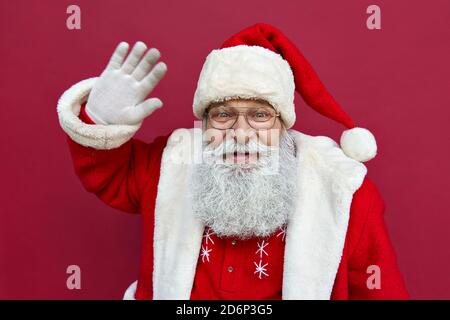 Joyeux Père Noël portant un costume en agitant la main en regardant la caméra. Banque D'Images