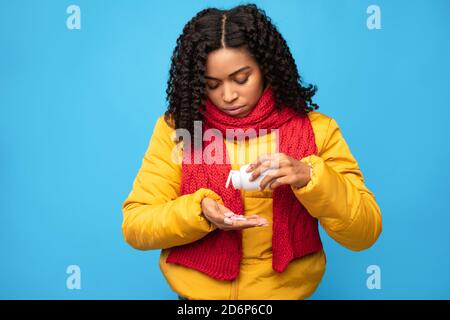 Malade Femme noire prenant des pilules traiter la grippe sur fond bleu Banque D'Images