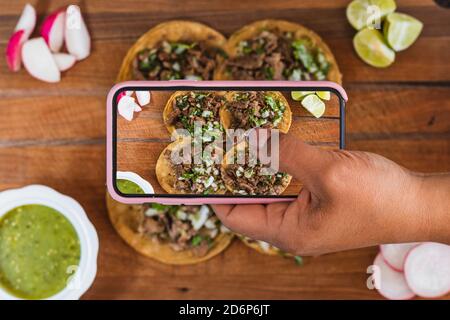 Personne photographiant des tacos mexicains et de la nourriture arranger sur une table. Femme hispanique main photographier le pasteur tacos à México. Banque D'Images