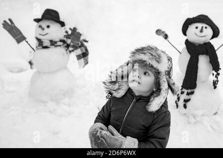 Bonhomme de neige et enfant drôle l'ami est debout dans un chapeau d'hiver et un foulard avec le nez rouge. Joyeux Noël et Bonne Année. Noël hiver enfants. Banque D'Images