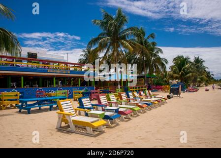 PLACENCIA, QUARTIER DE STANN CREEK / BELIZE - JUIN 2018: Chaises longues en bois coloré à l'extérieur de la plage Tipsy Tuna bar sur la plage de Placencia, Belize. Banque D'Images