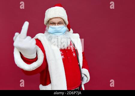 Le Père Noël porte un masque facial montrant le doigt du milieu sur fond rouge. Banque D'Images