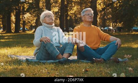 Concept de bien-être. Portrait d'un couple retraité senior heureux méditant dans le parc d'automne. Photo de haute qualité Banque D'Images