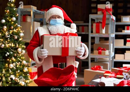 Le Père Noël portant un masque facial de costume tenant des cadeaux de Noël dans l'atelier. Banque D'Images