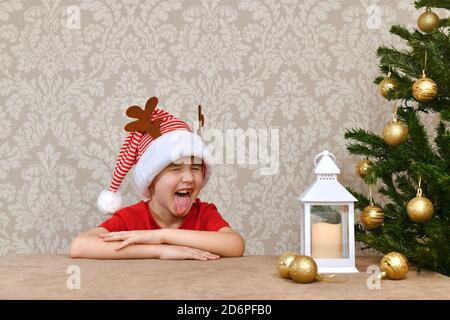 Un enfant dans un carnaval rayé rouge blanc chapeau gaiement writhes son visage et montre sa langue. Banque D'Images