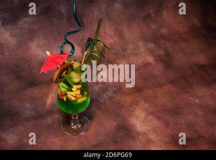 Un verre de jus vert à base de kiwi avec de la glace, des morceaux de fruits, une paille et un parapluie. Gros plan. Banque D'Images