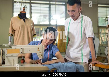 le tailleur masculin se tient à côté et voit la tailleur femelle utiliser la machine à coudre dans la salle de production Banque D'Images