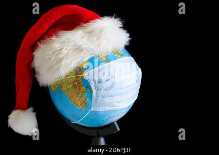 Globe terrestre en chapeau de Noël et masque médical stérile à arrière-plan noir Banque D'Images