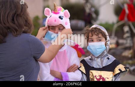 Une jeune fille en costume semble intraitable et très malheureuse alors que sa mère met un masque pour sa sécurité et sa protection. Covid-19 ruines Halloween. Banque D'Images