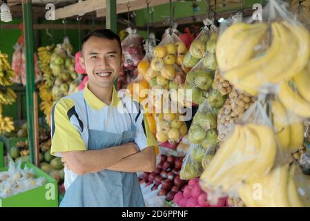 Portrait à la taille du jeune homme beau travaillant dans les fruits faites des achats et souriez à l'appareil photo tout en posant sur un porte-fruits Banque D'Images