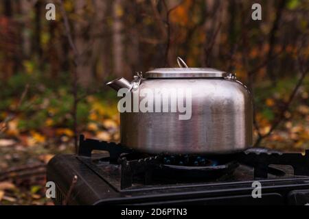 théière en métal argenté touristique sur un poêle à gaz portable dans la nature, dans la forêt, conditions de randonnée Banque D'Images