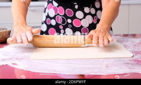 les mains des femmes roulent la pâte avec une broche sur une surface en bois, gros plan. les mains des femmes roulent la pâte sur une table de lilas. Les mains du chef s'en sont bien à la course Banque D'Images