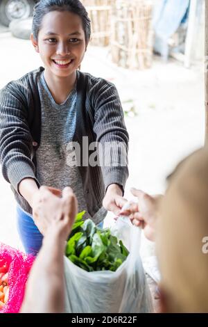 Gros plan d'une femme souriante tenant un sac en plastique rempli avec des légumes tout en faisant du shopping dans un magasin de légumes Banque D'Images