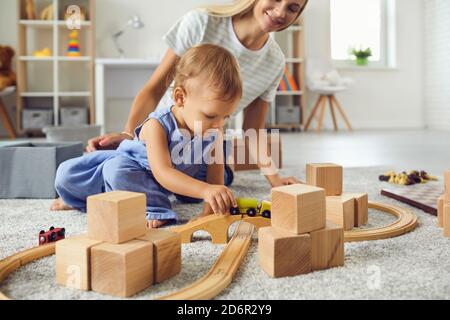 Jeune nounou et petit garçon jouant avec des blocs de bois dedans chambre moderne et confortable pour bébé Banque D'Images