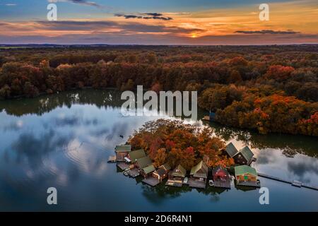 Tata, Hongrie - magnifique coucher de soleil d'automne sur des chalets de pêche en bois sur une petite île au lac Derito (Derito-to) en octobre. Panorama aérien Banque D'Images