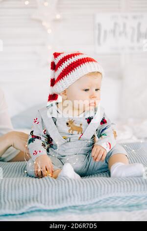 Le premier Noël de l'enfant. Le petit garçon triste pensif est allongé dans un costume de fête sur le lit dans une salle lumineuse.concept de Noël. Banque D'Images