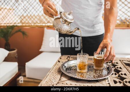 Homme tenant à la main une théière argentée vintage et versant le thé marocain sucré à la menthe traditionnel. Hospitalité et service arabes. Banque D'Images