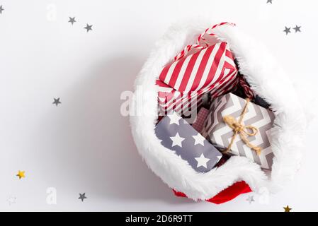 Arrière-plan de Noël avec chapeau de Père Noël rouge rempli de couleurs différentes boîtes-cadeaux et bonbons sur un fond gris clair décoré de brindilles de sapin vert, copie Banque D'Images