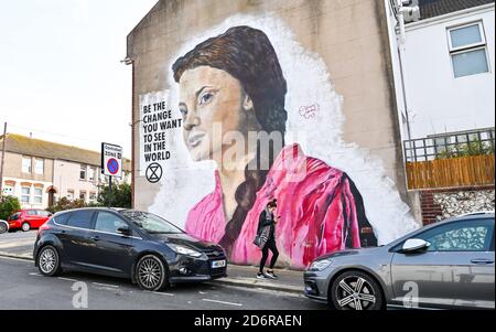 Brighton Royaume-Uni 19 octobre 2020 - UNE jeune femme passe devant une murale géante sur le changement climatique Greta Thunberg sur un mur dans la région de Queens Park à Brighton lors d'une brillante journée d'automne. Le temps devrait devenir plus changeant au cours des prochains jours avec le vent et la pluie prévus pour la plupart des parties du pays : crédit Simon Dack / Alamy Live News Banque D'Images