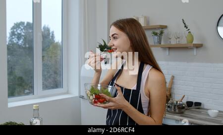 Jeune fille souriante mangeant de la salade de légumes frais crus posant à la cuisine ayant une émotion positive. Jeune fille sur le régime souriant appréciant un mode de vie sain. Nutrition concept végétarien éco-alimentaire Banque D'Images