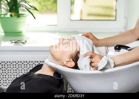 coiffeur couvre les cheveux du client avec une serviette. la jeune femme se lave les cheveux dans un salon de beauté Banque D'Images