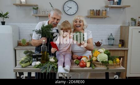 Blogueur enfant fille prenant des photos au téléphone avec des grands-parents de couple senior, faisant selfie à des comptes sociaux ou des histoires vidéo. Prendre des photos, prendre des selfies pour les médias sociaux sur smartphone dans la cuisine Banque D'Images