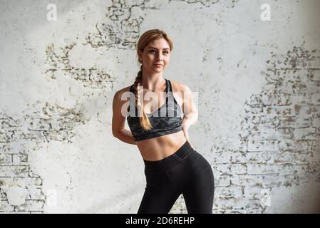 Jolie blonde est engagée dans la forme physique sur le fond d'un mur de brique blanche à la maison pendant la quarantaine. Restez à la maison et exercez votre corps. Banque D'Images