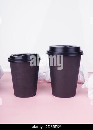 deux tasses de café en papier brun sur fond rose, papier froissé à côté. Banque D'Images